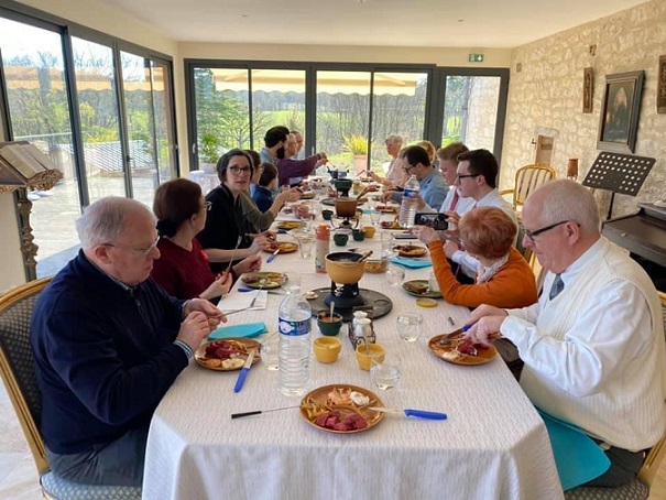 grande table avec 15 frères et soeurs chrétiens dégustant une fondu Suisse